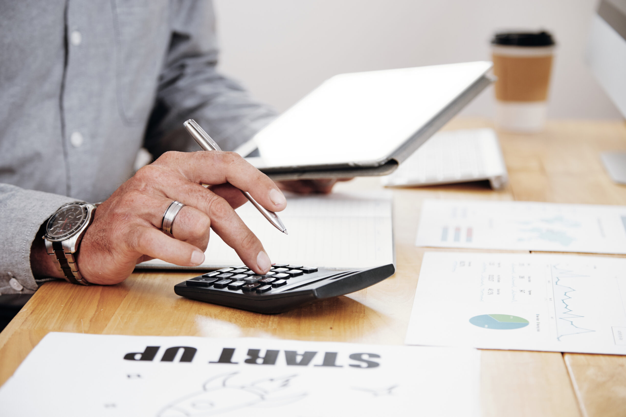 Close-up of businessman counting the profit of the company and using digital tablet at office desk